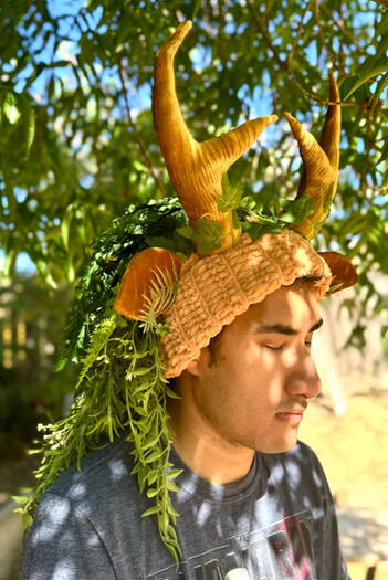 Thick golden-tan velvet crocheted beanie with matching golden velvet textured antlers and ears. Covered with various ferns and climbing green foliage.