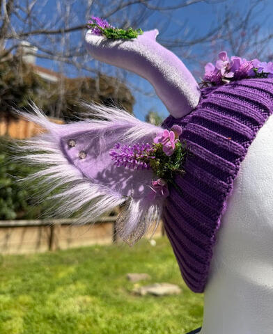 Warm toned purple beanie with pastel lavender antlers. Matching lavender ears with fluffy backing, silver earrings, and silver spike studs. Lavender sprouts with floofy moss from the ears and along the antlers.