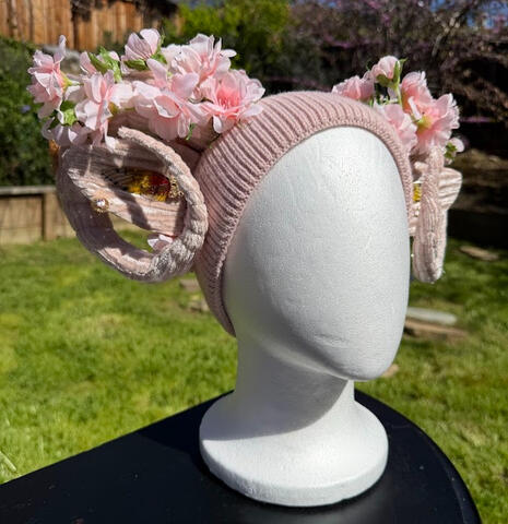 Light pink beanie with velvet light pink faun horns. Ballet pink roses adorn the horns with fluffy green moss. A golden lattice butterfly perches on both horns. Features matching pink ears with butterfly wing acrylic accents and golden earrings.