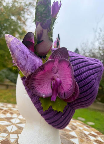 A purple orchid blooms at the base of the antlers and behind each ear. A purple/pink flower accents each antler.