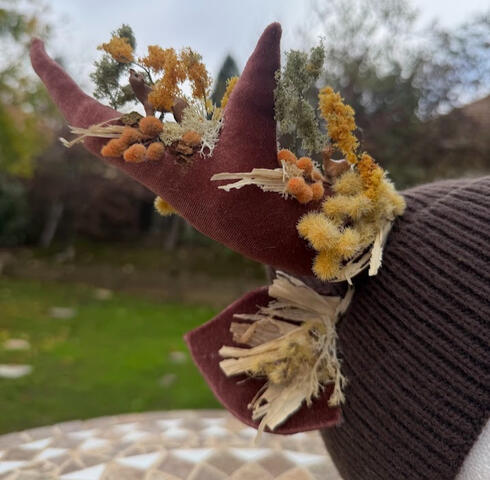 Birch Forest antlers of chestnut brown velvet fabric on a mousy brown (unlined) beanie. Stalks of wheat line the antlers&#39; forest line along with autumnal plant accents. A family of deer, a wolf, and a cougar can be discovered along the forest line.
