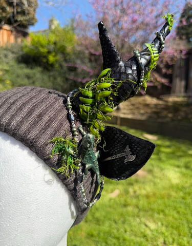 A horned lizard painted deep metallic green crawls on either side of the beanie. Silver axes stem from each ear, battle ready. Antlers are poseable, ears are pierceable &amp; bendable. Beanie has plush fleece lining for xtra comfort.