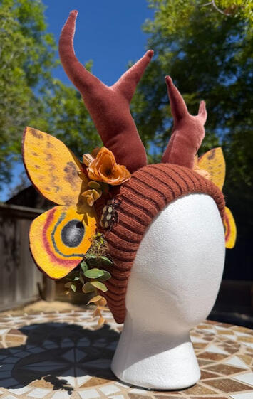 Io Moth wings are made of thick felt, painted with acrylic, and heat-set once dry. Wings are semi poseable with inner wire. Faux florals of autumnal shades decorate around the antlers and wings. Moth wings have a matching velvet backing.